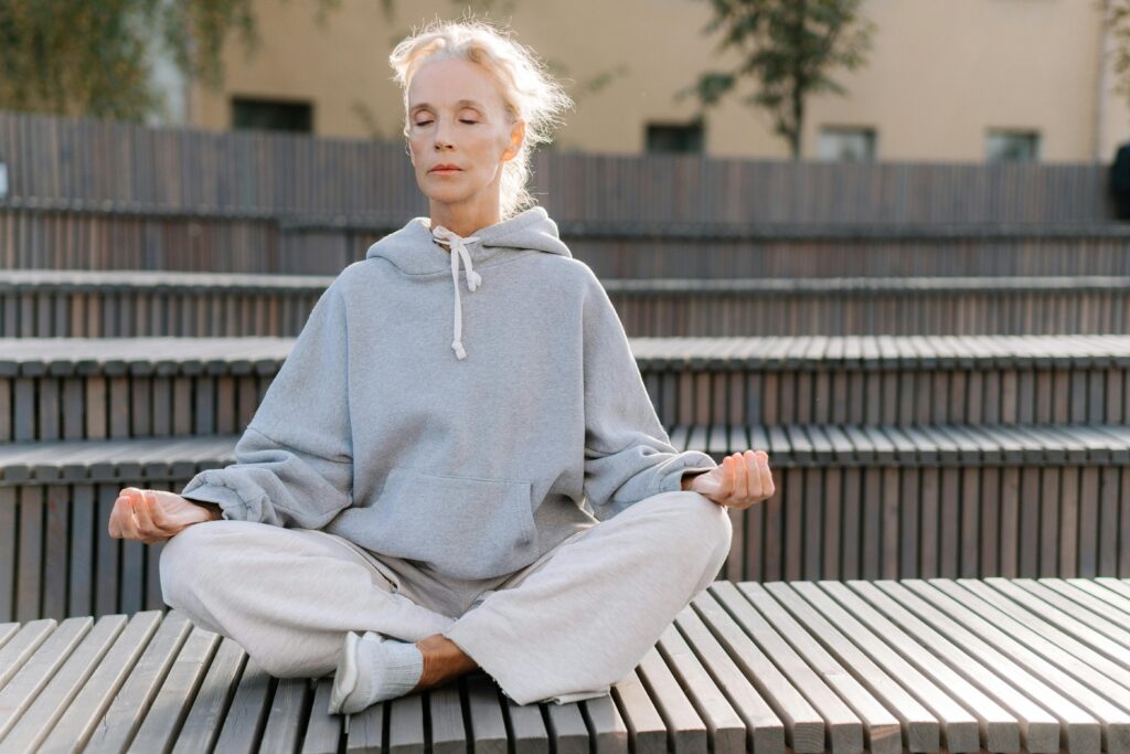 Elderly woman in gray hoodie meditating outdoors